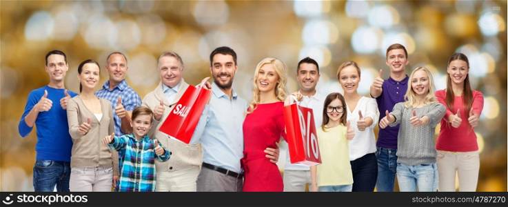 sale, family, generation and people concept - group of happy men and women with shopping bags showing thumbs up over holidays lights background