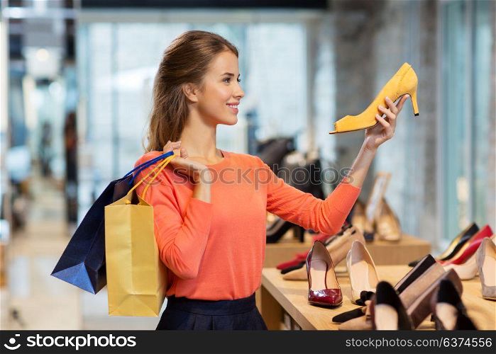 sale, fashion and people concept - happy young woman with shopping bags choosing shoes at store. happy young woman choosing shoes at store