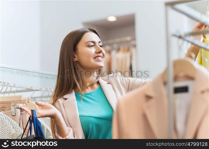 sale, fashion, consumerism and people concept - happy young woman with shopping bags choosing clothes in mall or clothing store