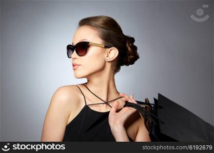 sale, fashion, people and luxury concept - happy beautiful young woman in black sunglasses with shopping bags over gray background
