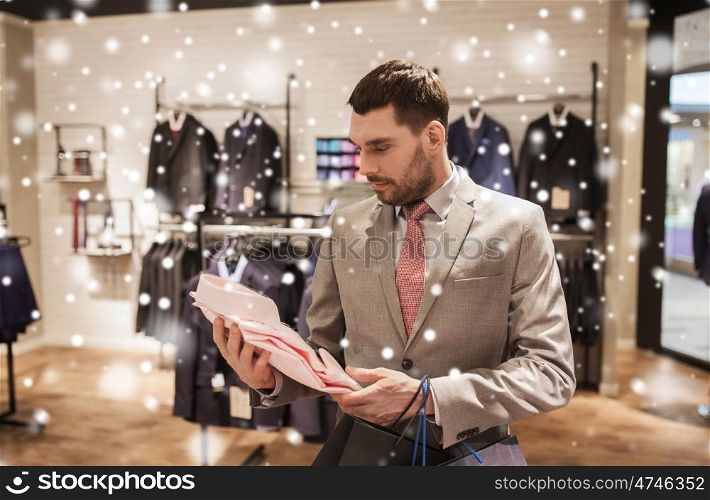 sale, fashion, style and people concept - elegant young man or businessman in suit with shopping bags choosing shirt in mall or clothing store over snow