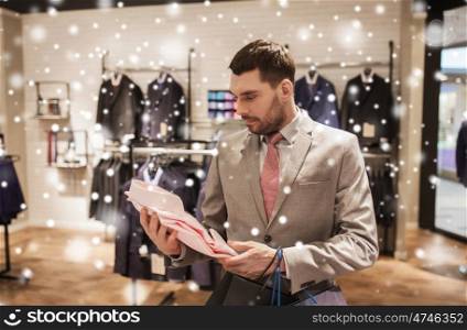 sale, fashion, style and people concept - elegant young man or businessman in suit with shopping bags choosing shirt in mall or clothing store over snow