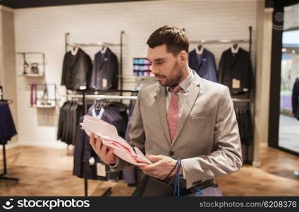 sale, fashion, style and people concept - elegant young man or businessman in suit with shopping bags choosing shirt in mall or clothing store