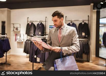 sale, fashion, style and people concept - elegant young man with shopping bags in suit choosing shirt in mall or clothing store