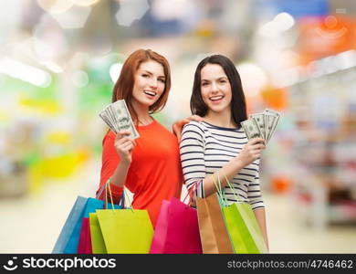 sale, finances and people concept - two smiling teenage girls with shopping bags and cash money over supermarket background
