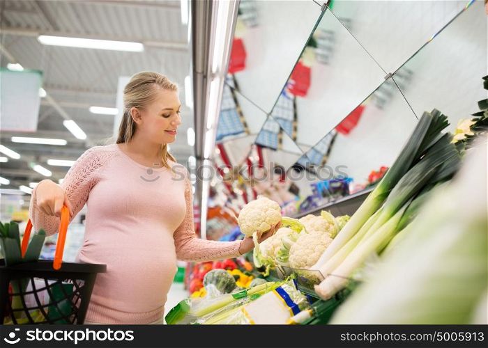 sale, food, pregnancy and people concept - happy pregnant woman with shopping basket buying cauliflower at grocery store or supermarket. happy pregnant woman buying cauliflower at grocery