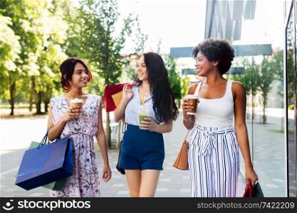 sale, friendship and people concept - happy young women with shopping bags and takeaway drinks walking along city street. women with shopping bags and drinks in city