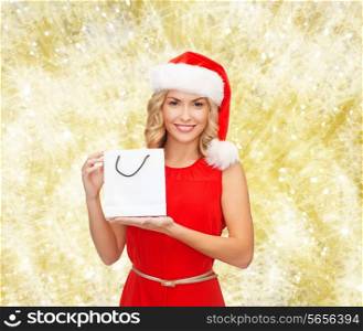 sale, gifts, christmas, holidays and people concept - smiling woman in red dress and santa helper hat with white blank shopping bag over yellow lights background
