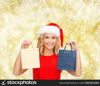 sale, gifts, christmas, holidays and people concept - smiling woman in red dress and santa helper hat with shopping bags over yellow lights background