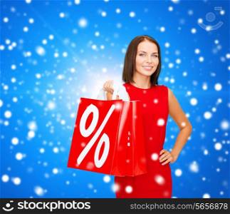 sale, gifts, christmas, holidays and people concept - smiling woman in red dress with shopping bags and percent sign over blue snowy background