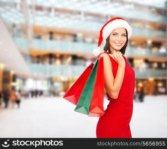 sale, gifts, christmas, holidays and people concept - smiling woman in red dress with shopping bags over shopping center background