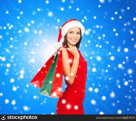 sale, gifts, christmas, holidays and people concept - smiling woman in red dress with shopping bags over blue snowy background