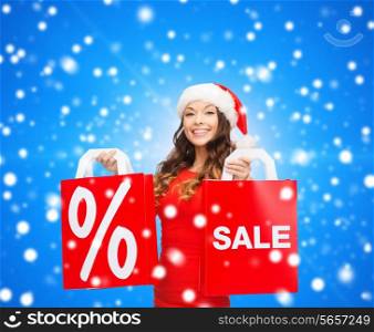 sale, gifts, christmas, holidays and people concept - smiling woman in red dress with shopping bags and percent sign on them over blue snowy background
