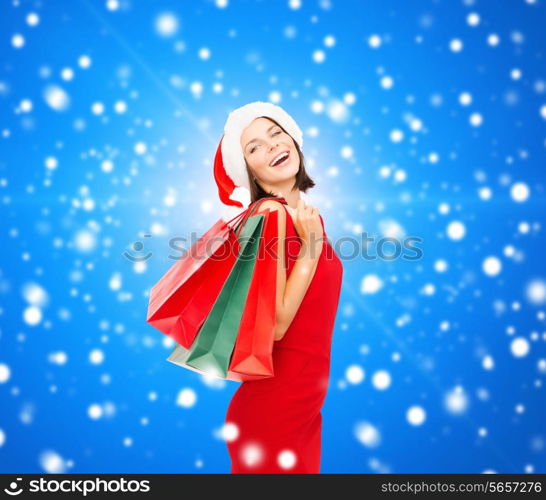 sale, gifts, christmas, holidays and people concept - smiling woman in red dress with shopping bags over blue snowy background