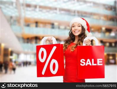 sale, gifts, christmas, holidays and people concept - smiling woman in red dress with shopping bags and percent sign on them over shopping center background