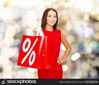 sale, gifts, christmas, holidays and people concept - smiling woman in red dress with shopping bags and percent sign over lights background