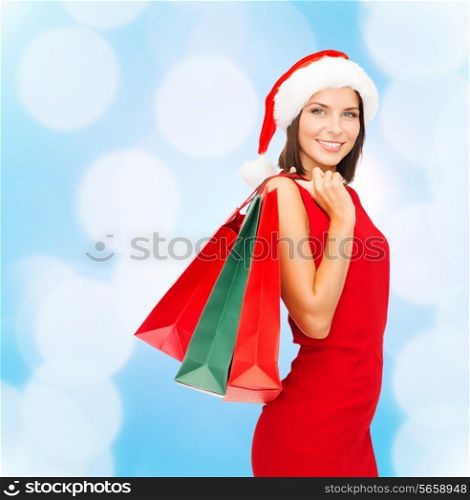 sale, gifts, christmas, holidays and people concept - smiling woman in red dress with shopping bags over blue lights background