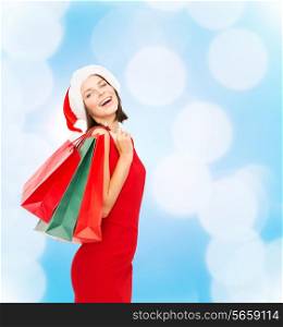 sale, gifts, christmas, holidays and people concept - smiling woman in red dress with shopping bags over blue lights background