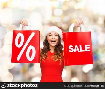 sale, gifts, christmas, holidays and people concept - smiling woman in red dress with shopping bags and percent sign on them over lights background