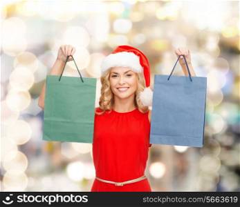 sale, gifts, christmas, holidays and people concept - smiling woman in red dress and santa helper hat with shopping bags over lights background