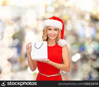 sale, gifts, christmas, holidays and people concept - smiling woman in red dress and santa helper hat with white blank shopping bag over lights background