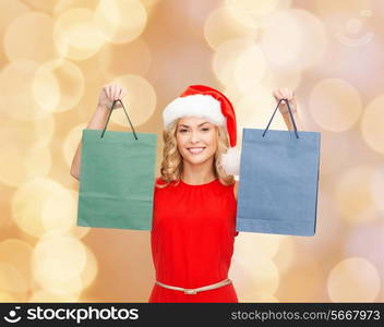 sale, gifts, christmas, holidays and people concept - smiling woman in red dress and santa helper hat with shopping bags over beige lights background