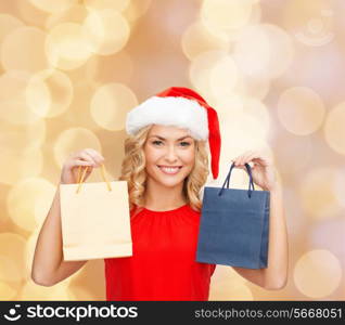 sale, gifts, christmas, holidays and people concept - smiling woman in red dress and santa helper hat with shopping bags over beige lights background