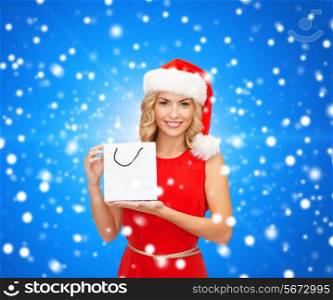 sale, gifts, christmas, holidays and people concept - smiling woman in red dress and santa helper hat with white blank shopping bag over blue lights background