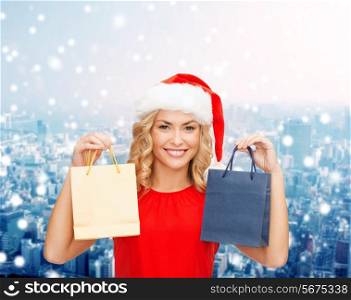 sale, gifts, christmas, holidays and people concept - smiling woman in red dress and santa helper hat with shopping bags over snowy city background