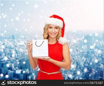 sale, gifts, christmas, holidays and people concept - smiling woman in red dress and santa helper hat with white blank shopping bag over snowy city background