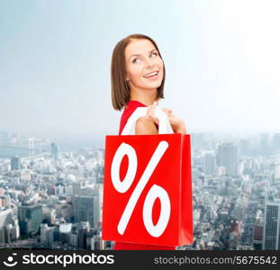 sale, gifts, christmas, holidays and people concept - smiling woman in red dress with shopping bags and percent sign over city background