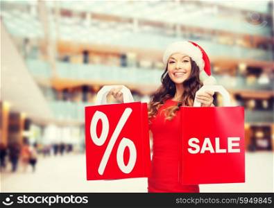 sale, gifts, christmas, holidays and people concept - smiling woman in red dress with shopping bags and percent sign on them over shopping center background