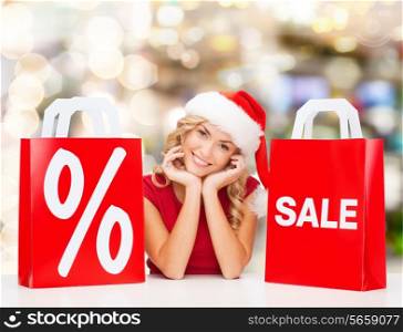 sale, gifts, christmas, holidays and people concept - smiling woman in santa helper hat with shopping bags and percent sign over lights background