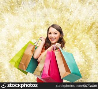 sale, gifts, christmas, holidays and people concept - smiling woman with colorful shopping bags over yellow lights background