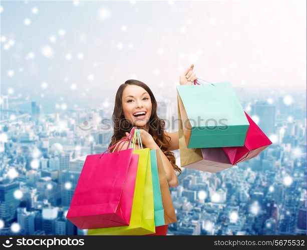 sale, gifts, christmas, holidays and people concept - smiling woman with colorful shopping bags over snowy city background