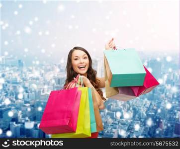 sale, gifts, christmas, holidays and people concept - smiling woman with colorful shopping bags over snowy city background