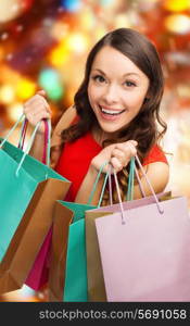 sale, gifts, christmas, holidays and people concept - smiling woman with colorful shopping bags over red lights background