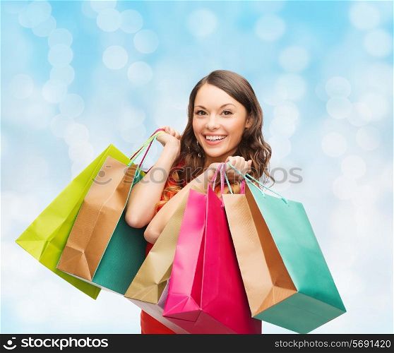 sale, gifts, christmas, holidays and people concept - smiling woman with colorful shopping bags over blue lights background