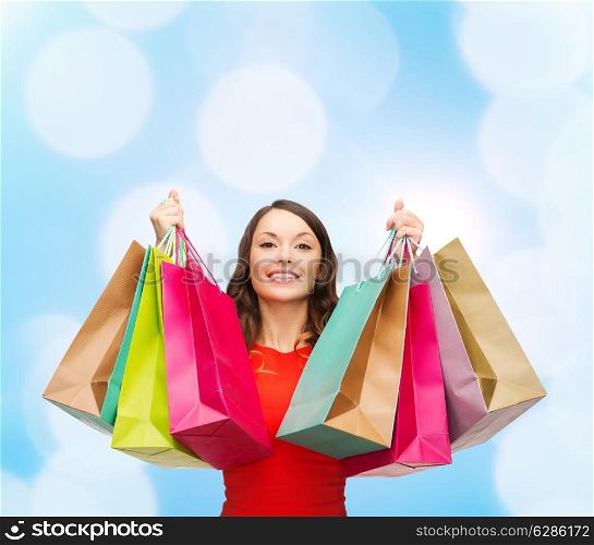 sale, gifts, christmas, holidays and people concept - smiling woman with colorful shopping bags over blue lights background