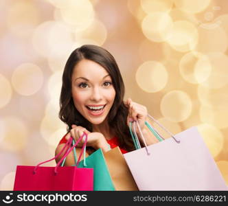 sale, gifts, christmas, holidays and people concept - smiling woman with colorful shopping bags over beige lights background