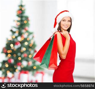 sale, gifts, holidays and people concept - smiling woman in red dress with shopping bags over living room and christmas tree background