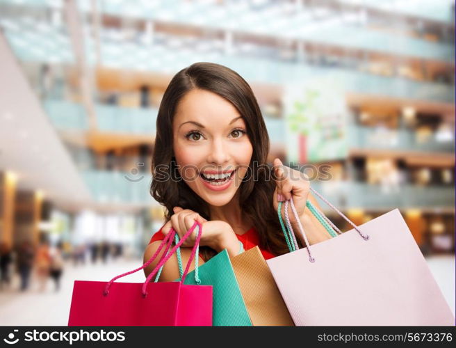 sale, gifts, holidays and people concept - smiling woman with colorful bags over shopping center background