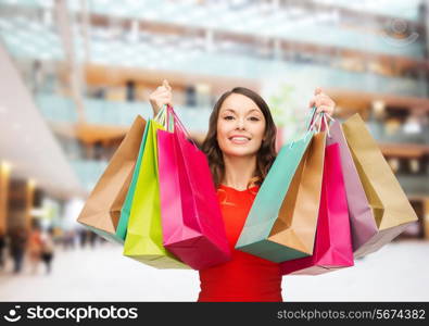 sale, gifts, holidays and people concept - smiling woman with colorful bags over shopping center background