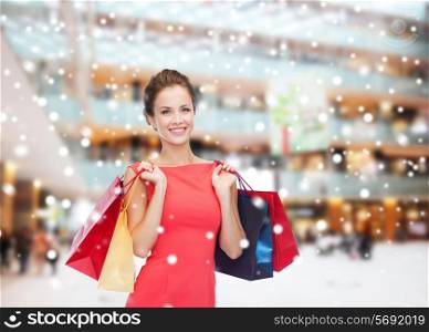 sale, gifts, holidays and people concept - smiling woman with colorful bags over shopping center background