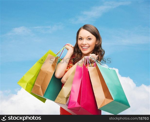 sale, gifts, holidays and people concept - smiling woman with colorful shopping bags over blue sky and cloud background