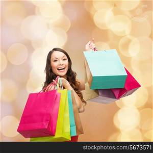 sale, gifts, holidays and people concept - smiling woman with colorful shopping bags over beige lights background