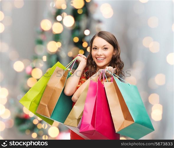sale, gifts, holidays and people concept - smiling woman with colorful shopping bags over living room and christmas tree background