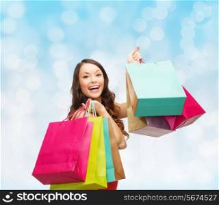 sale, gifts, holidays and people concept - smiling woman with colorful shopping bags over blue lights background