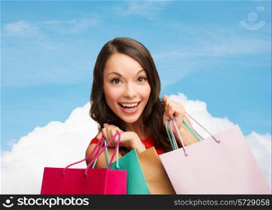 sale, gifts, holidays and people concept - smiling woman with colorful shopping bags over blue sky and cloud background