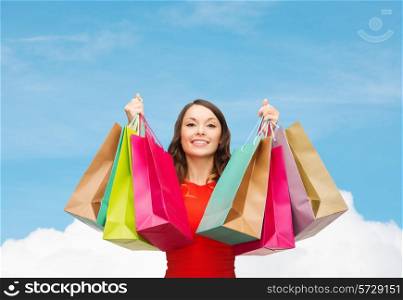 sale, gifts, holidays and people concept - smiling woman with colorful shopping bags over blue sky and white cloud background